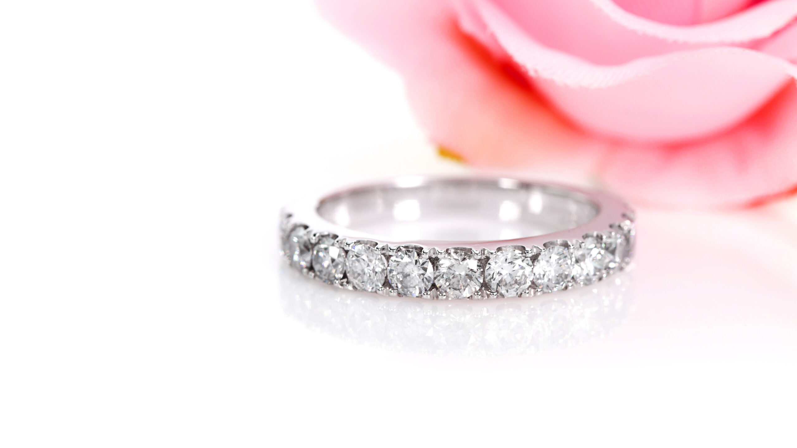A classic diamond eternity, sitting on a white background with a rose behind. Shop classic diamond eternity rings below.
