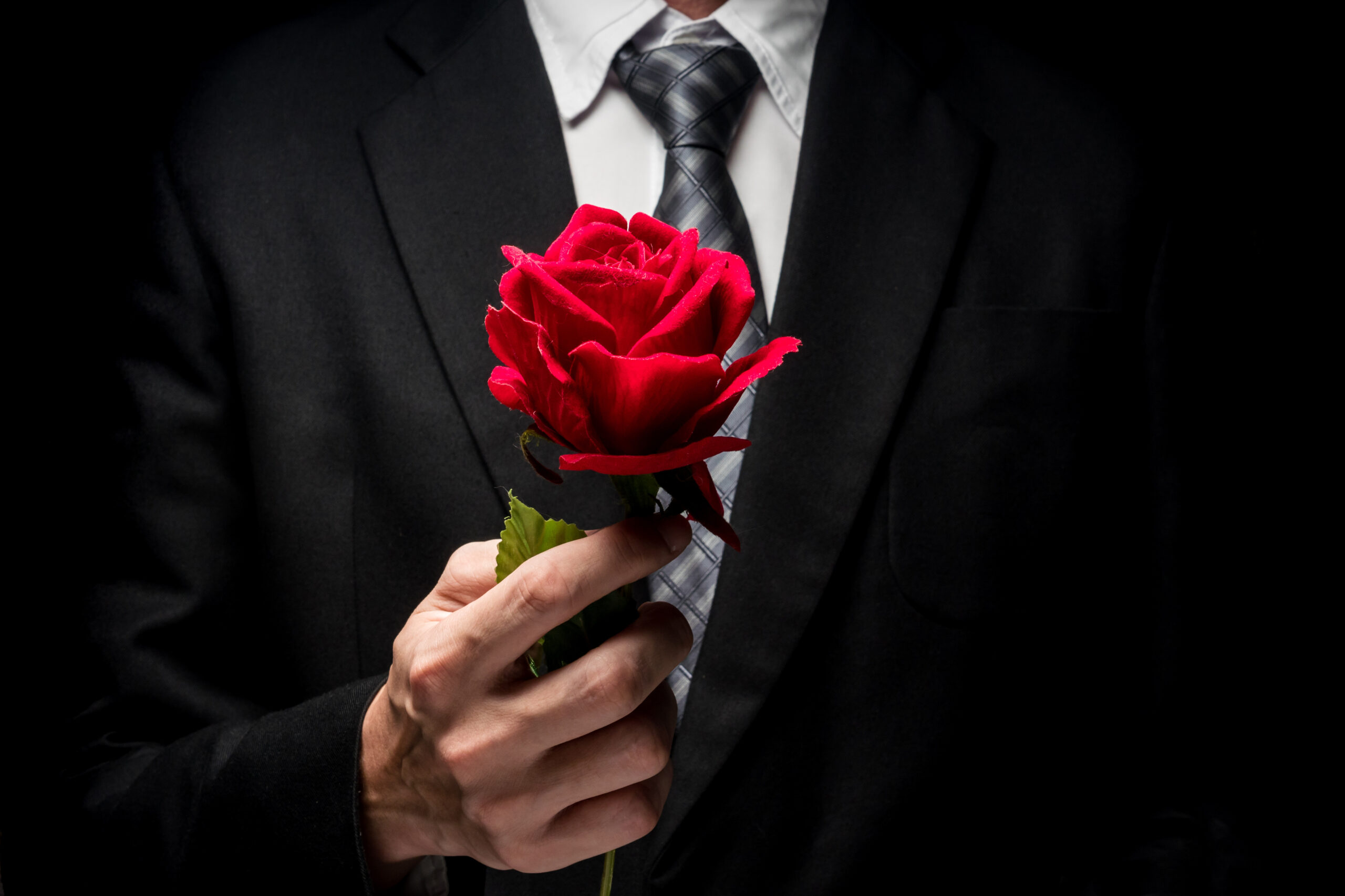close up of man in black suit holding red rose.